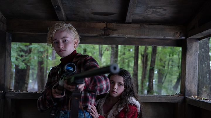 Wolf Man (2025) film still of actors, Julia Garner holding the rifle and Matilda Firth